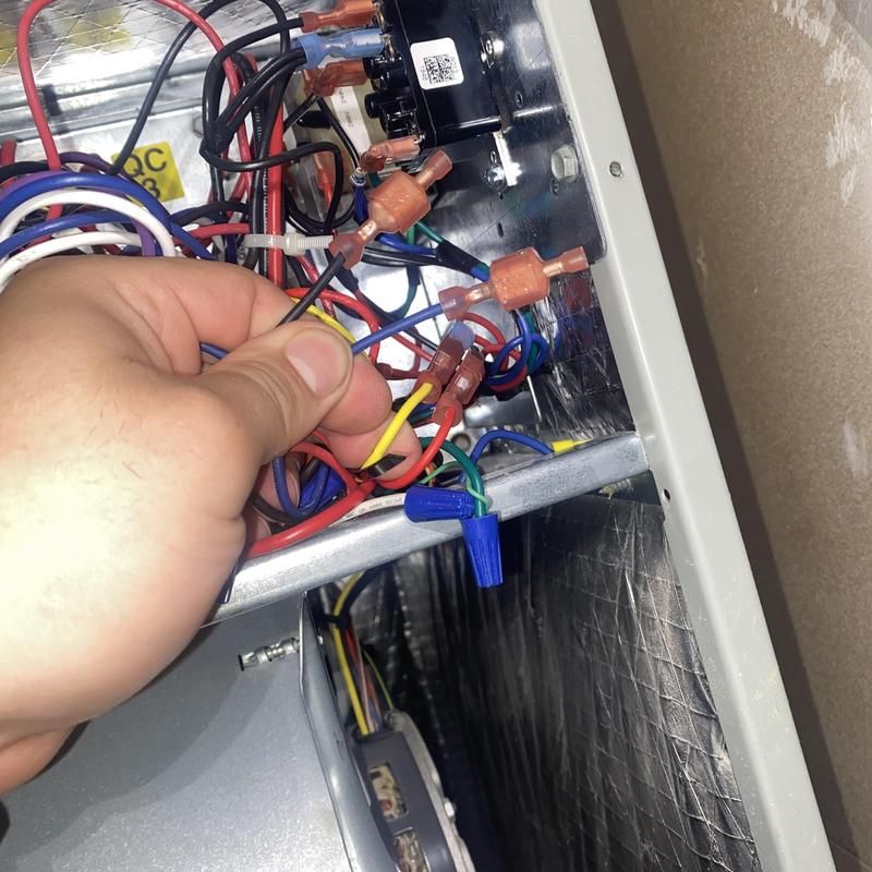 Hand connecting electrical wires inside a furnace. Wires are various colors.