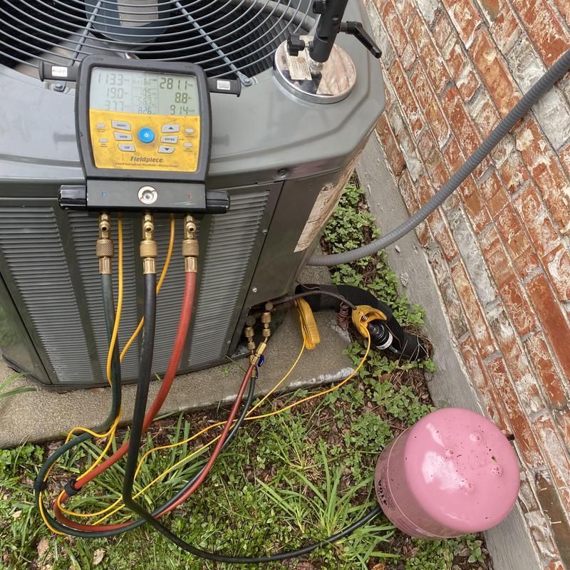 AC unit being serviced outdoors; gauges attached. Pink tank, brick wall.
