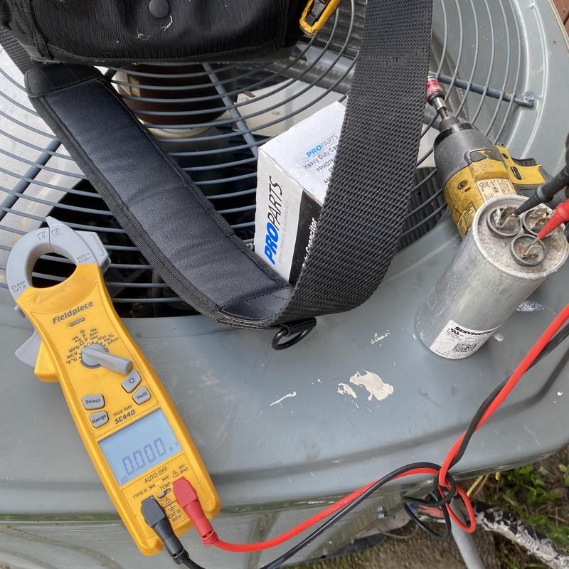 A yellow multimeter with black and red probes connected to an HVAC capacitor.