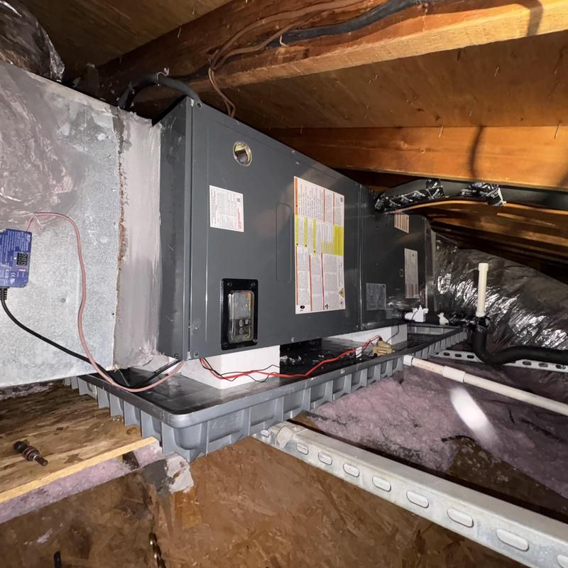HVAC unit installed in an attic. Gray metal box with connected ductwork, electrical wiring, and a control box.