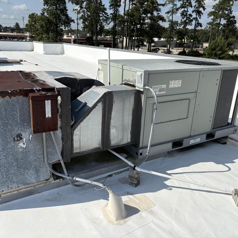 Rooftop HVAC unit with ductwork; on white roof, overcast sky.