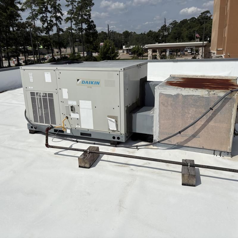 Large Daikin HVAC unit on a white rooftop with metal piping and an older unit nearby.