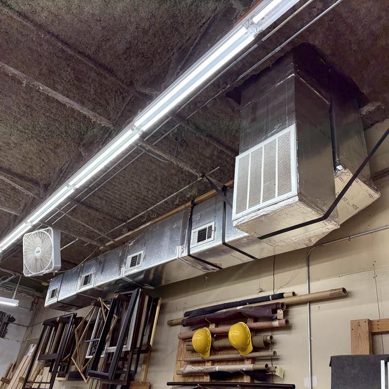Ventilation system and lights in a workshop, featuring metal ductwork, a fan, and safety helmets.