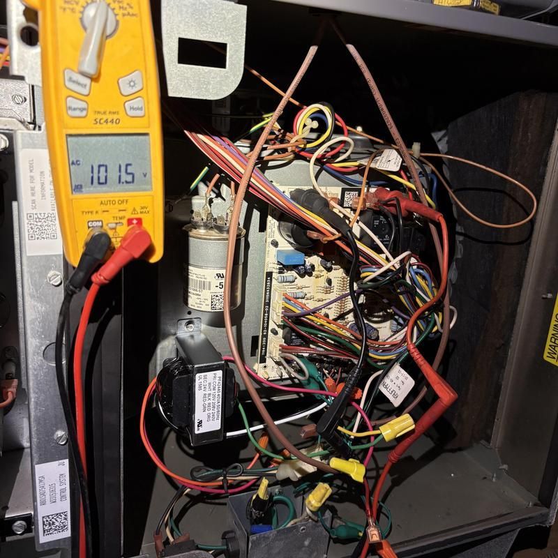 A technician tests wiring of a furnace with a multimeter, showing 101.5 volts.