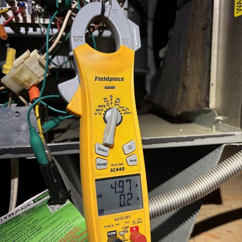 Yellow clamp meter measuring electrical current on HVAC system wiring.