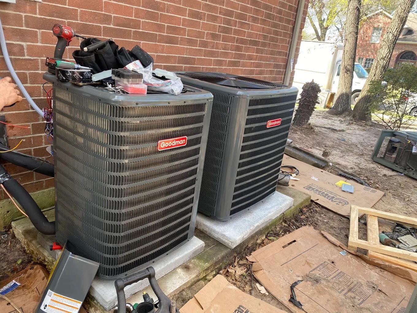 Two Bryant air conditioning units outside a brick building. Tools rest on top of one unit.