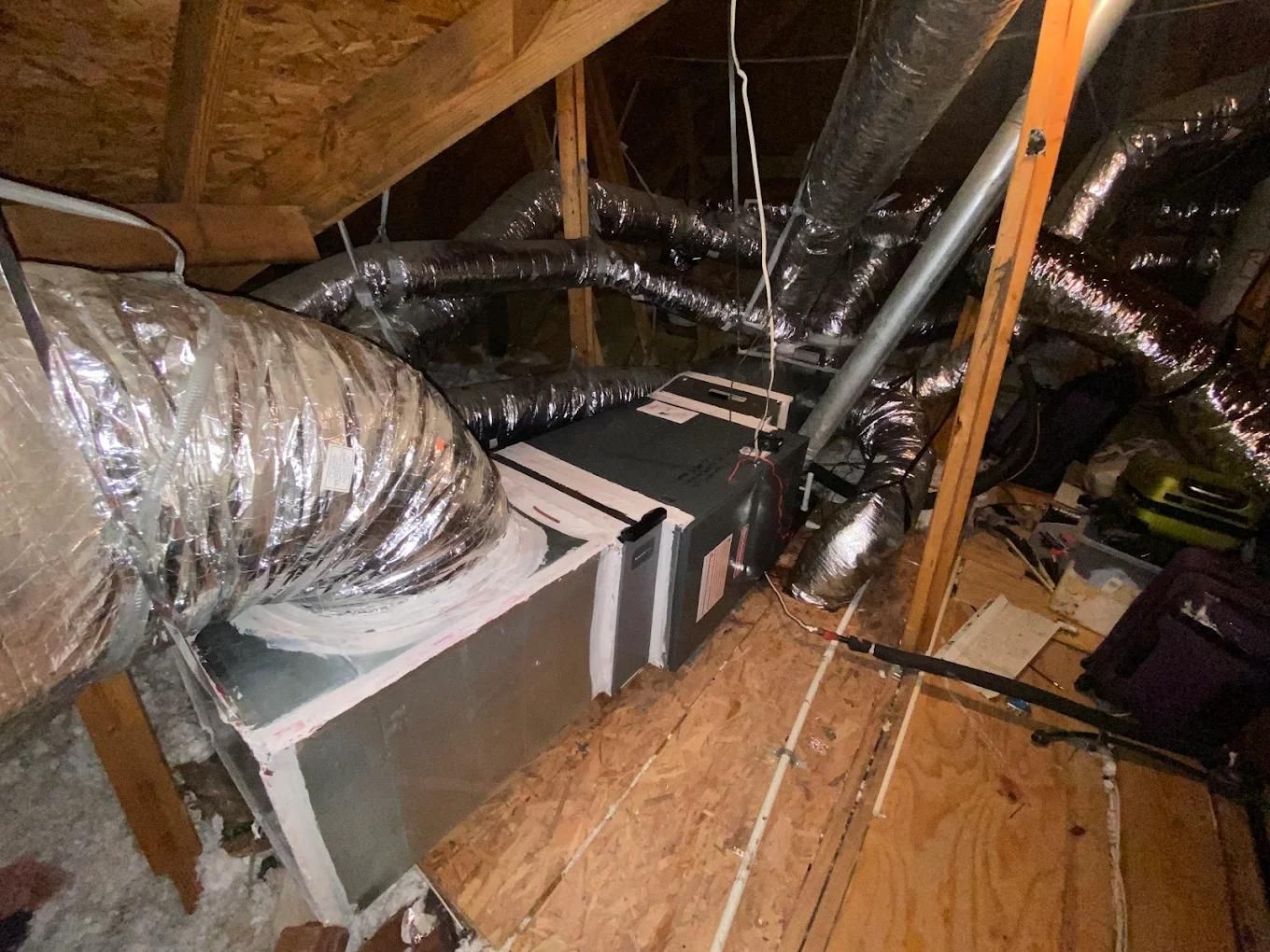 HVAC system in an attic with ducts. Silver metal box with ducts connected, on wooden boards.