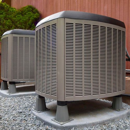 Two outdoor air conditioning units on concrete pads in a backyard.