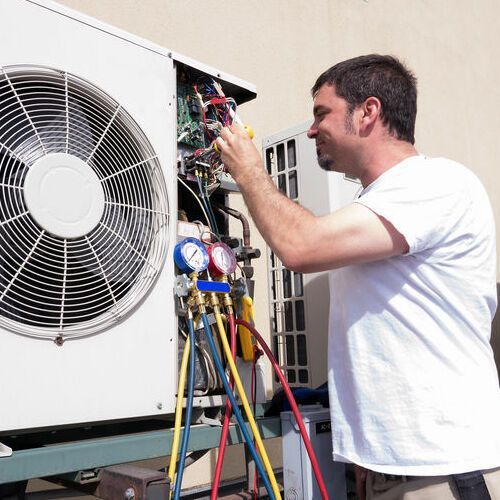 Man repairing an air conditioning unit outdoors, using gauges and tools; smiling.