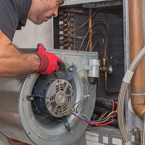 Man in red gloves inspecting HVAC unit, focusing on fan motor and wiring.
