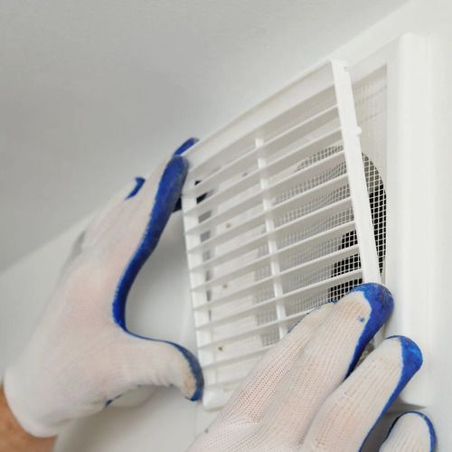 Person wearing gloves removing a white vent cover from a white wall.