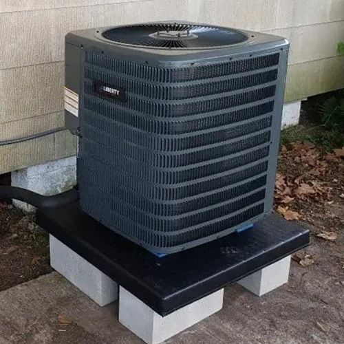 Air conditioning unit on a platform of cinder blocks, set against a house.