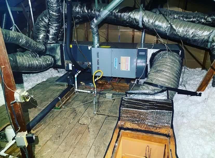 HVAC system in an attic, with insulated ductwork, wooden beams, and a rectangular unit with labels.