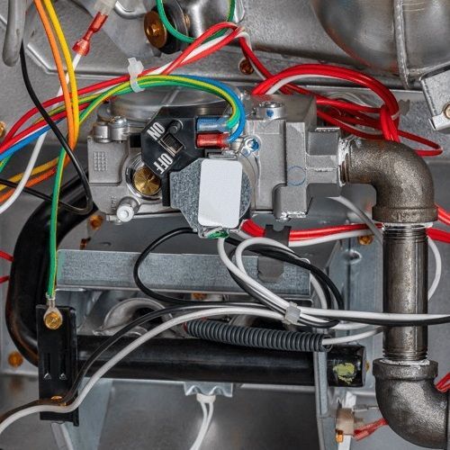 Close-up of furnace components: gas valve, wiring, pipes, and a burner assembly.