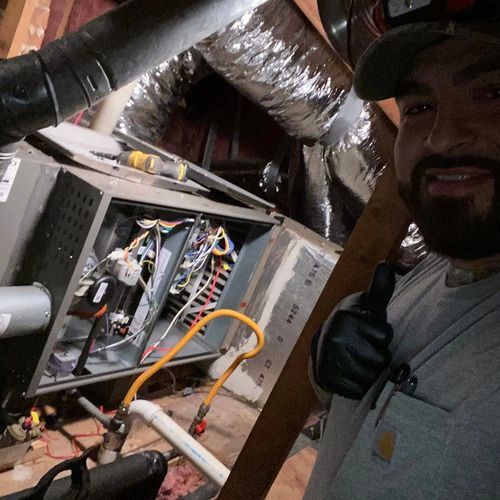 HVAC technician in attic, working on a furnace with tools. Smiling, giving a thumbs up.