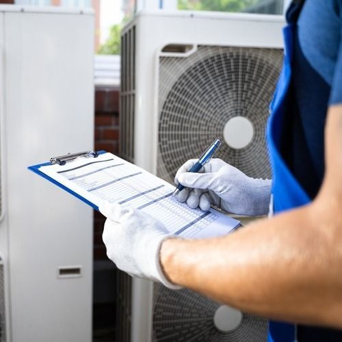 HVAC technician in gloves writing on a checklist in front of air conditioning units.
