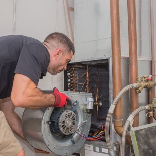 Man in black shirt and red gloves repairs HVAC unit, inspecting components.