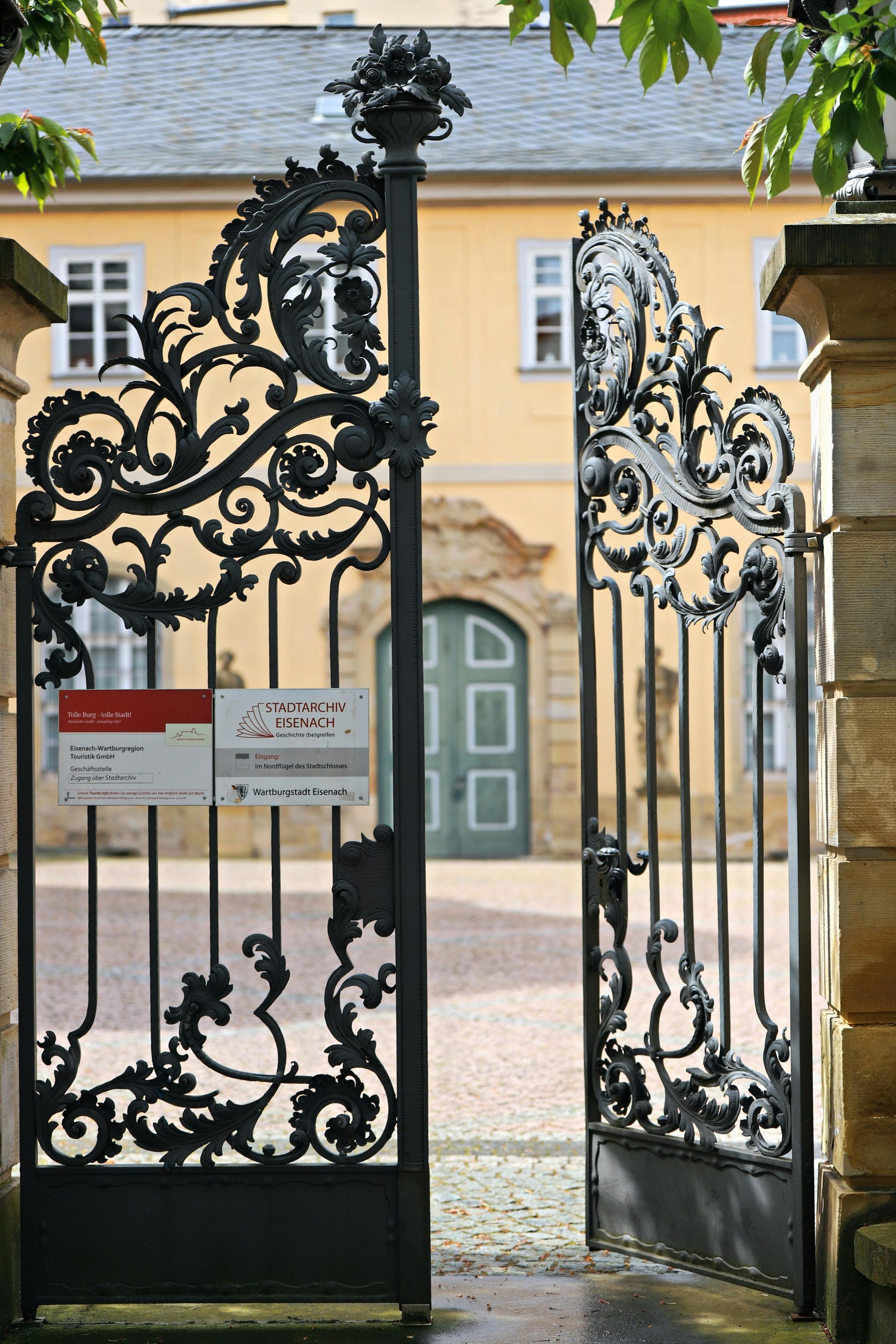 A wrought iron gate is open to a yellow building