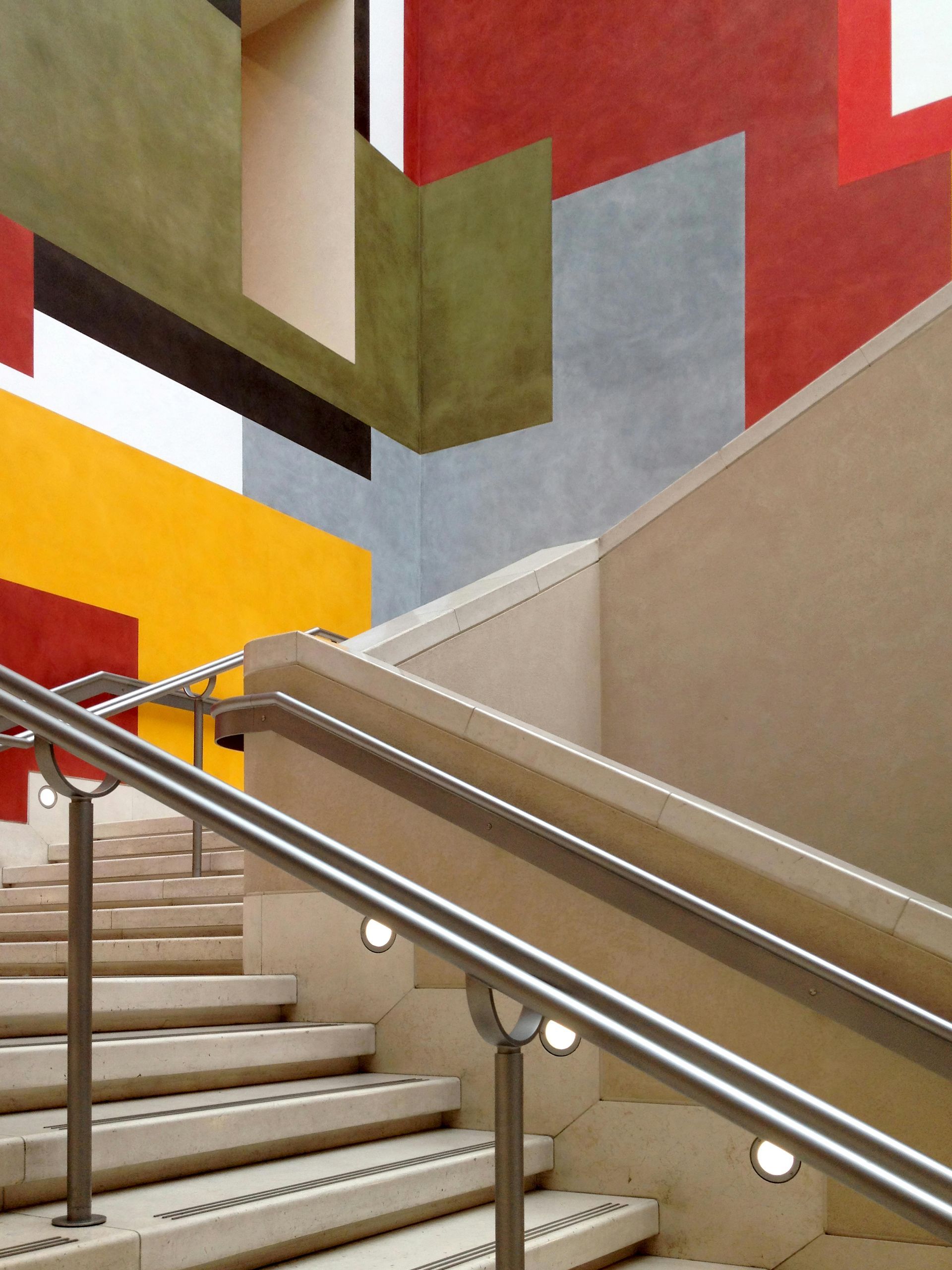 A staircase with a metal railing and a colorful wall behind it