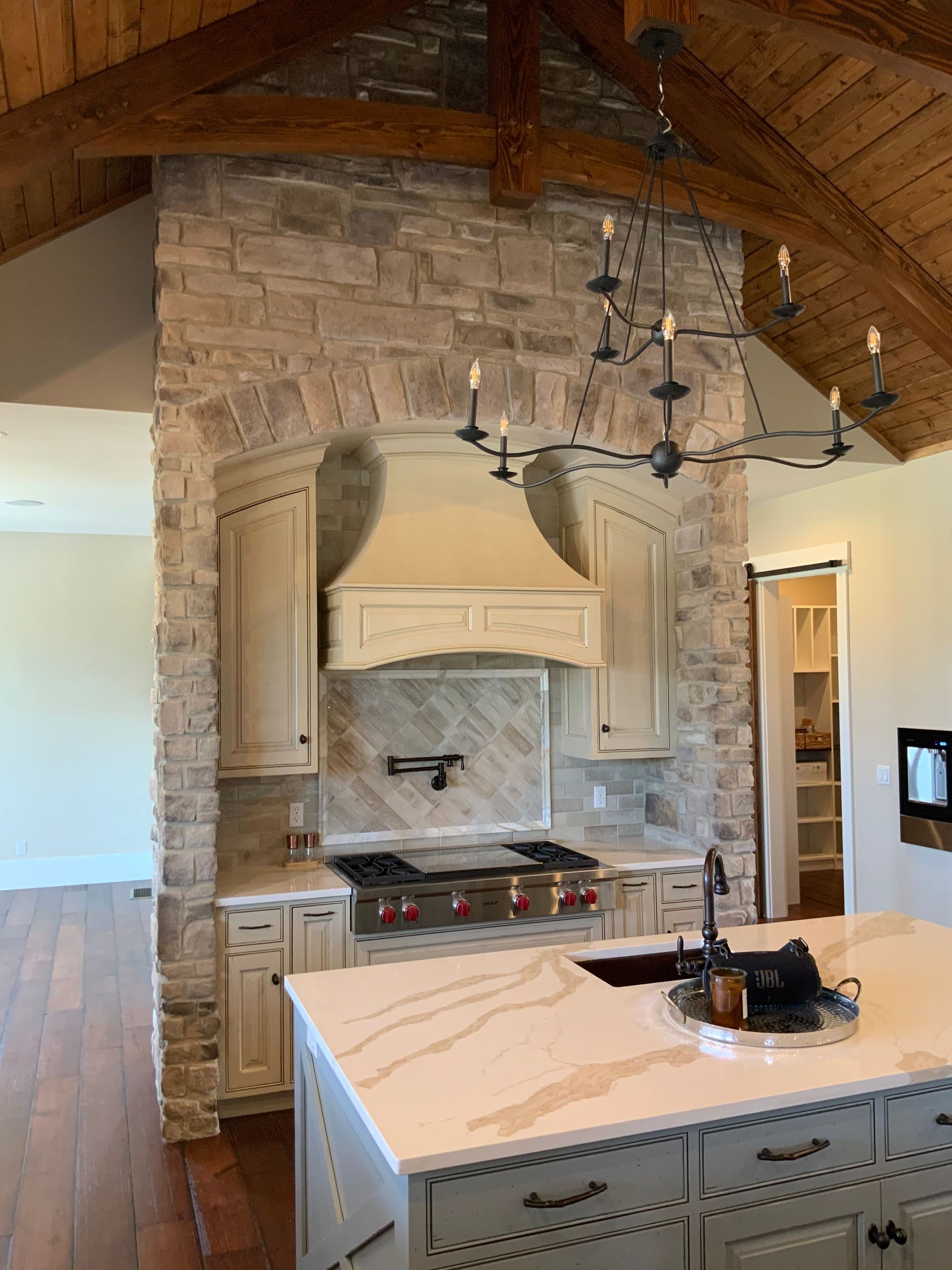 A kitchen with a stove , sink , cabinets and a brick wall.