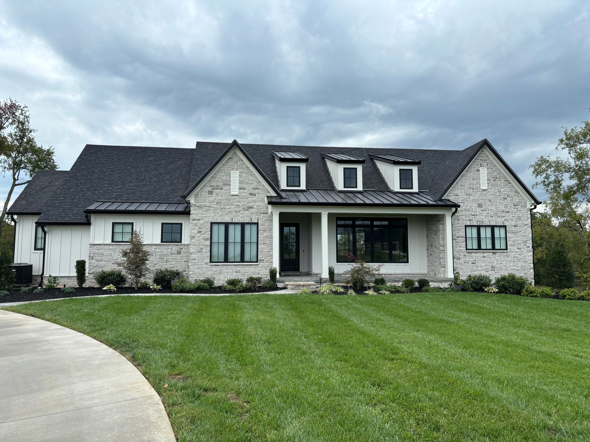 A large white house with a black roof is sitting on top of a lush green lawn.