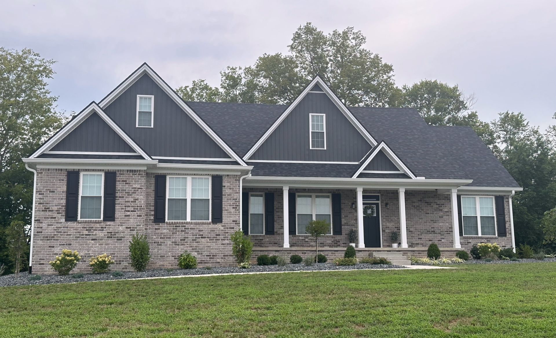 A large brick house with a black roof is sitting on top of a lush green field.