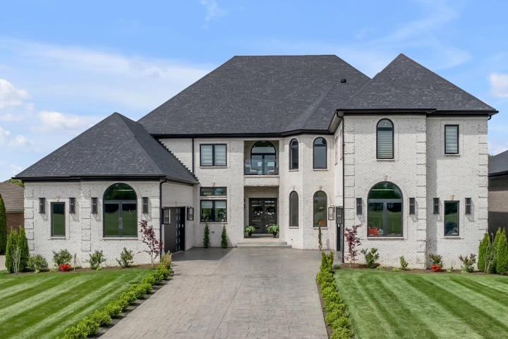 A large white house with a gray roof and a driveway leading to it.