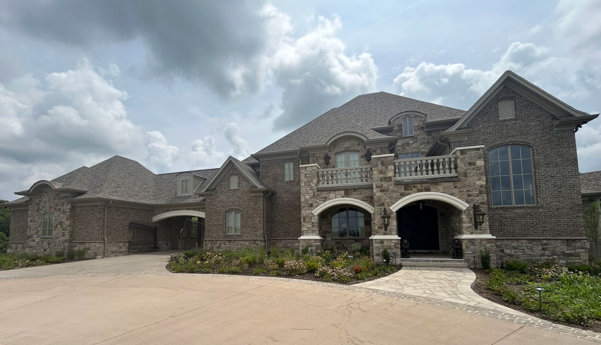 A large stone house with a driveway in front of it on a cloudy day.