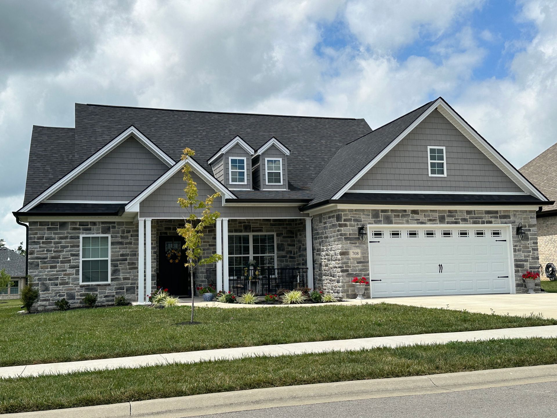 A large stone house with a gray roof and a white garage door.