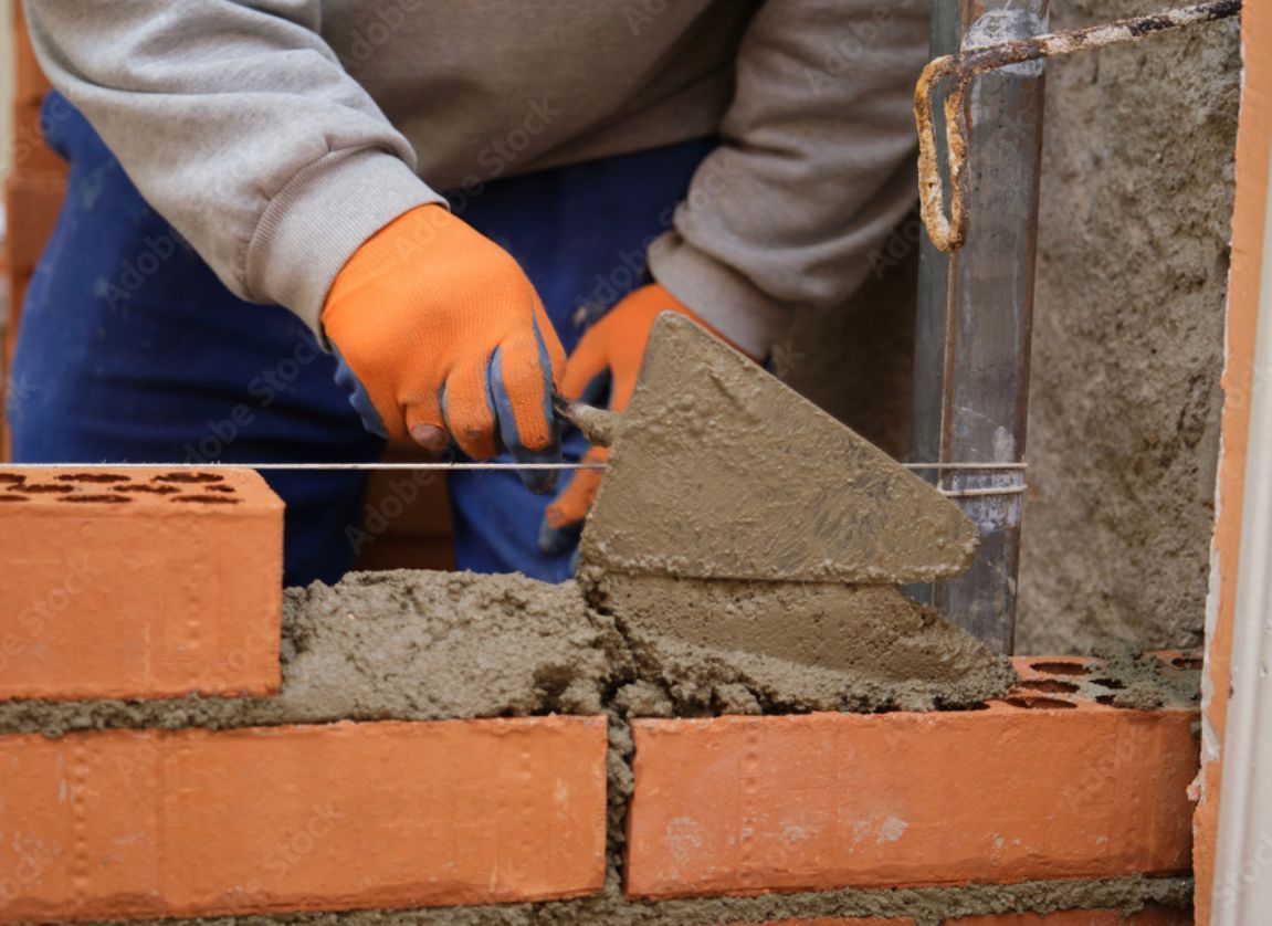 a man wearing orange gloves is laying bricks on a wall .