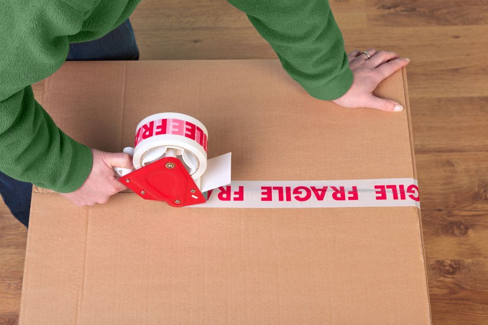 A Person is Taping a Cardboard Box With Fragile Tape — Ballina Removals & Storage in Ballina, NSW
