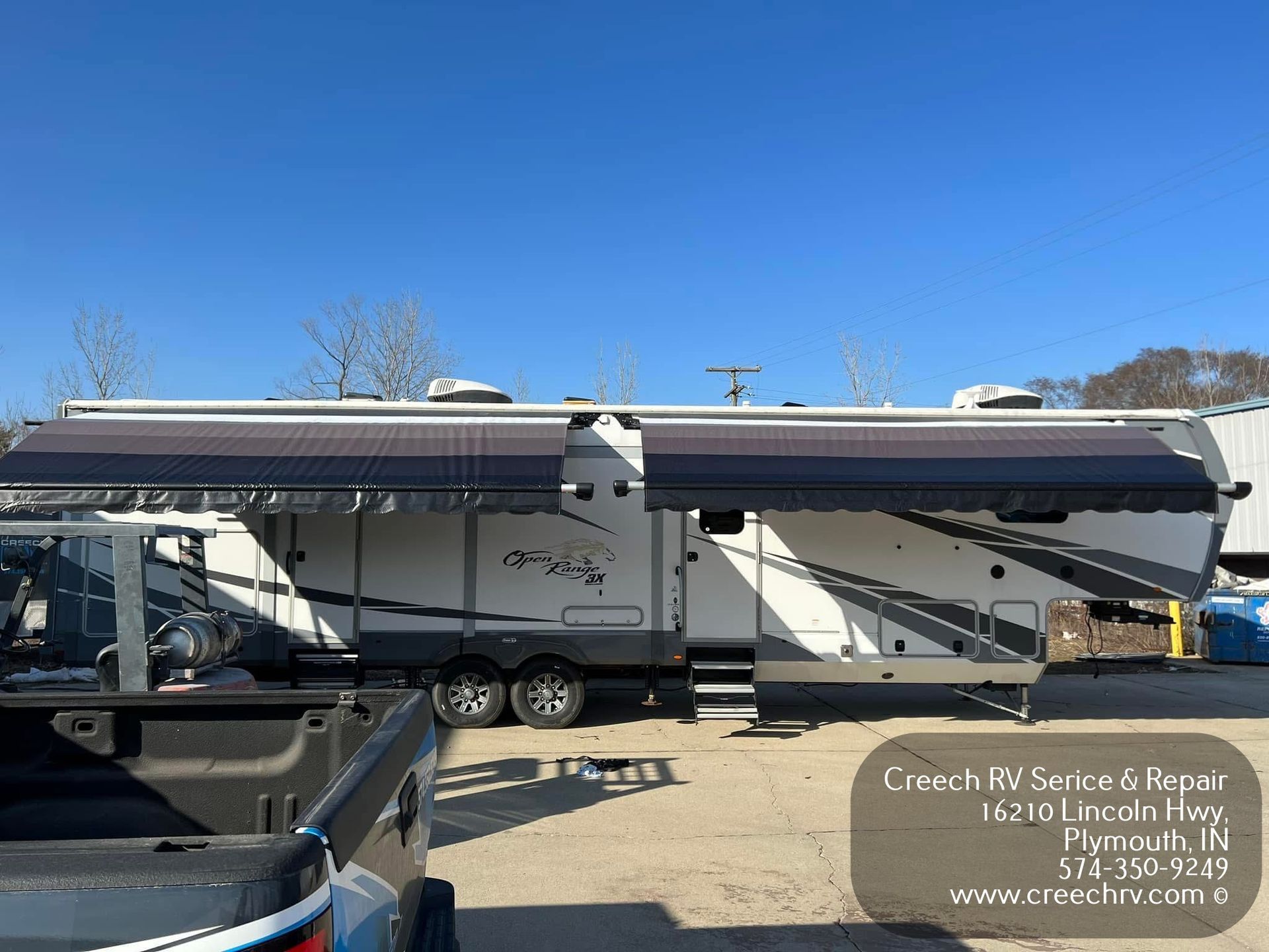 White RV with awning extended, parked on asphalt. Creech RV Service & Repair sign is visible.