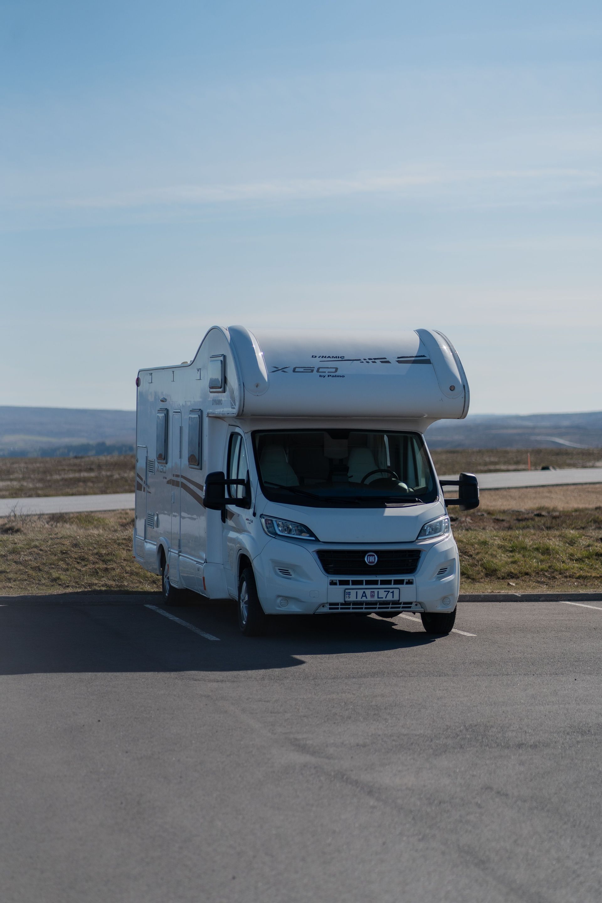 White camper van parked on a paved lot near a body of water under a clear blue sky
