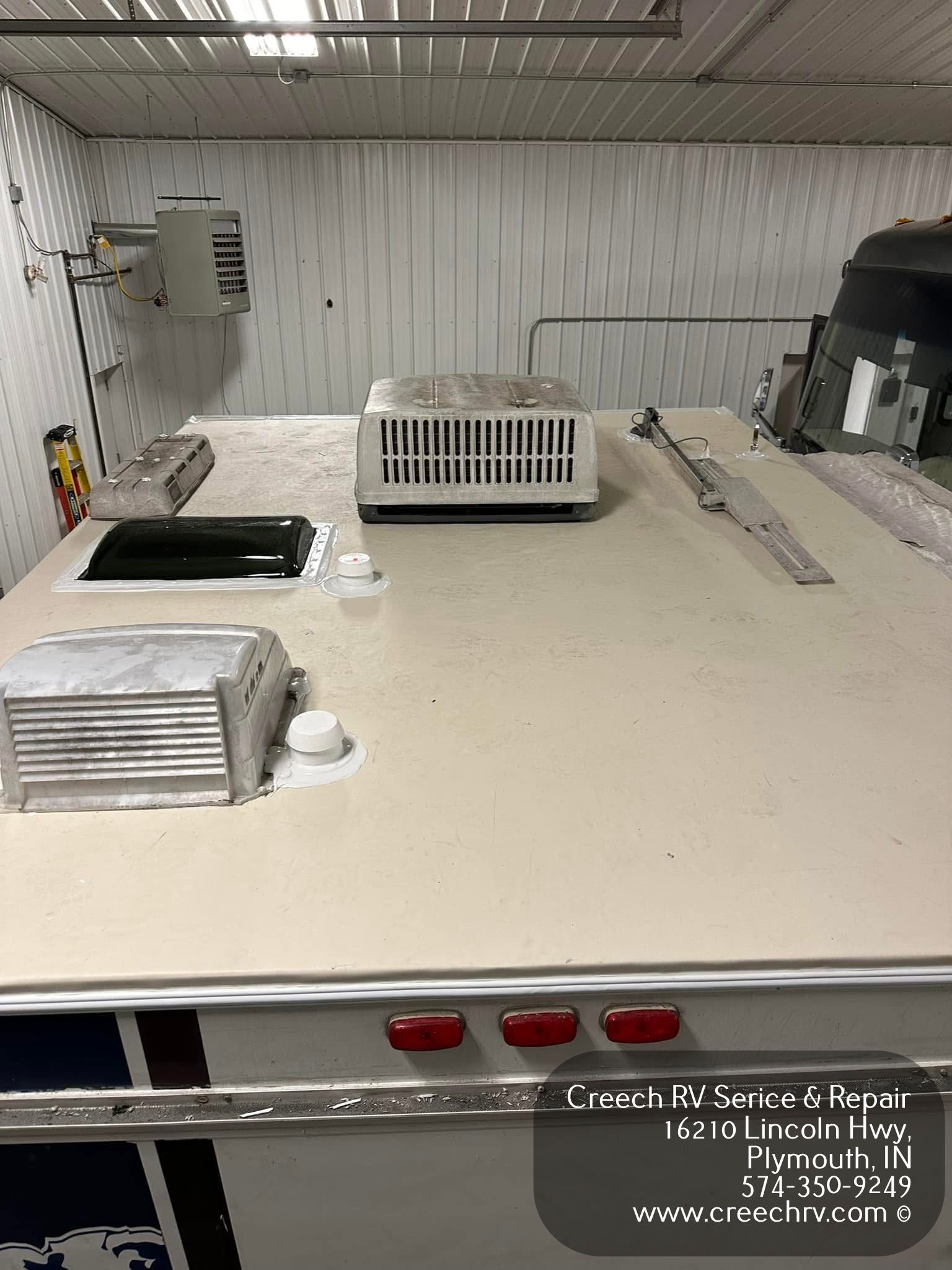 RV roof with air conditioner, vents, and sealant in a repair shop.