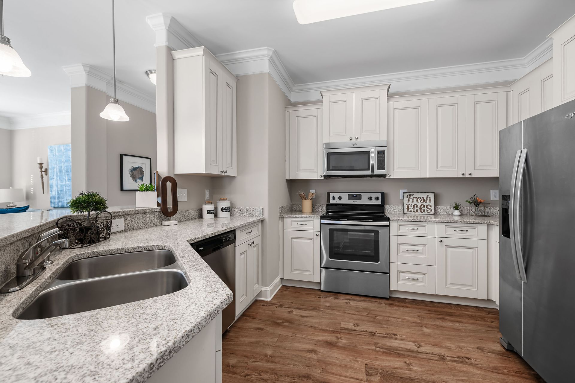 A kitchen with white cabinets , stainless steel appliances , granite counter tops and hardwood floors at Marquis Ellis Crossing offers apartments for rent in Durham, NC.