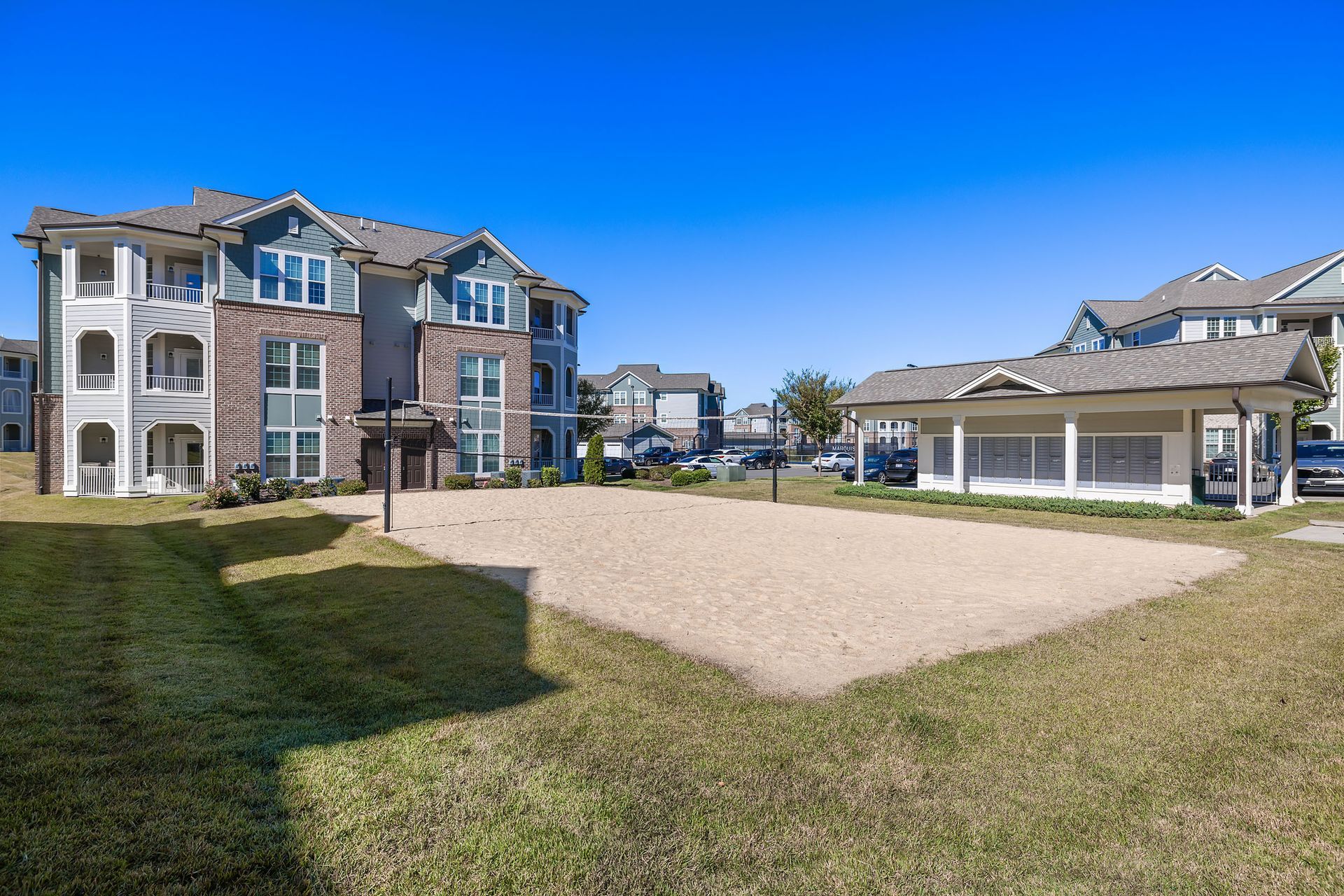 There is a volleyball court in the middle of a grassy field in front of a building at Marquis Ellis Crossing offers apartments in Durham, NC.
