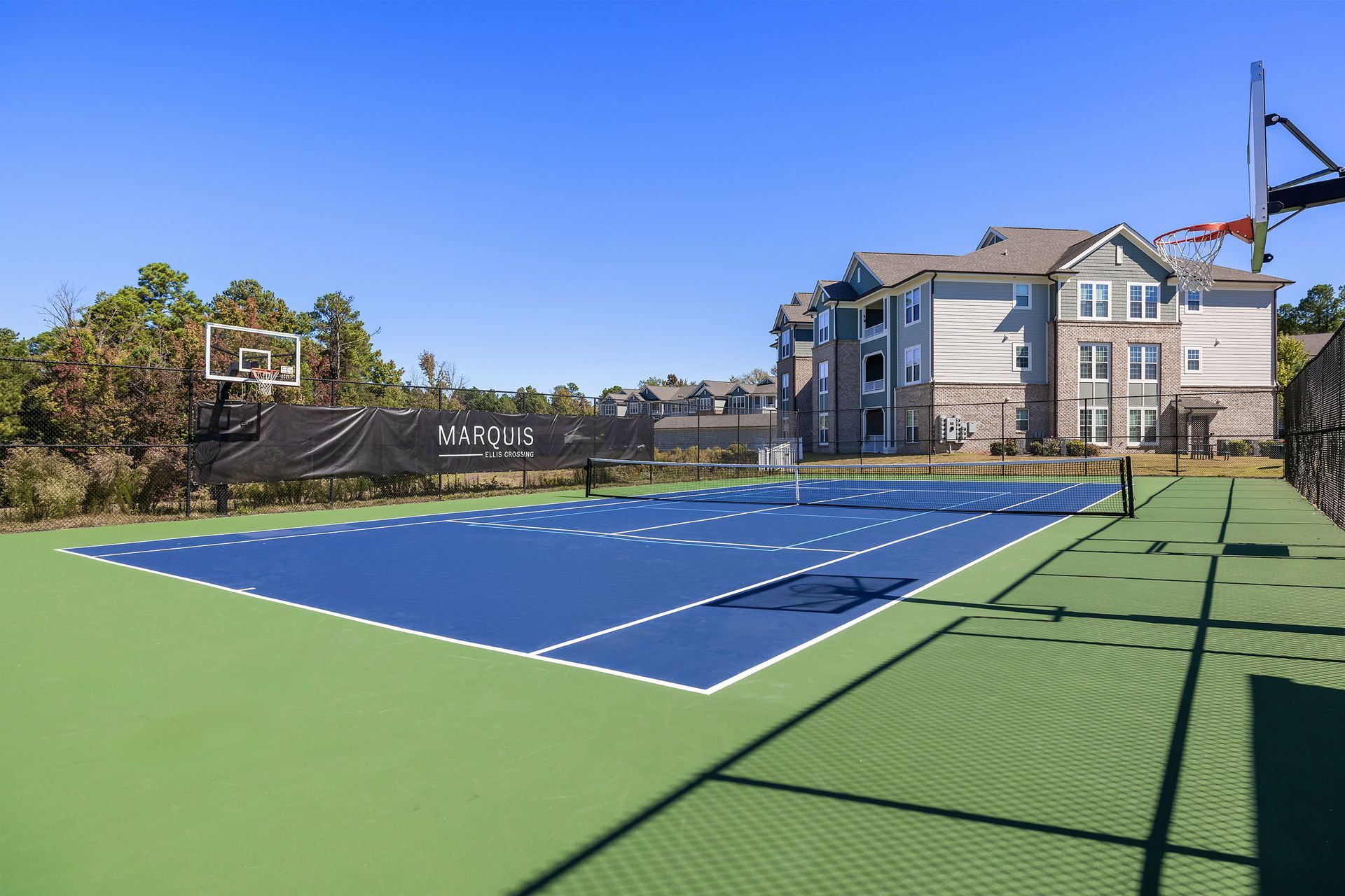 A tennis court with a basketball hoop in front of a building at Marquis Ellis Crossing offers apartments for rent in Durham, NC.