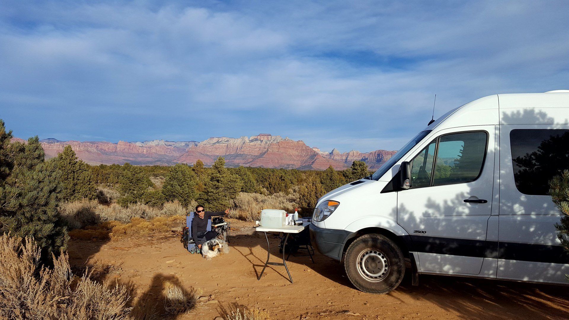 White Sprinter van with a camp table outside and a girl sitting on a camp chair