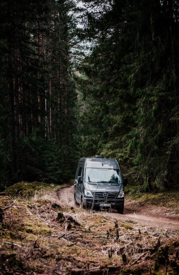 Sprinter Van driving on a dirt road through the woods