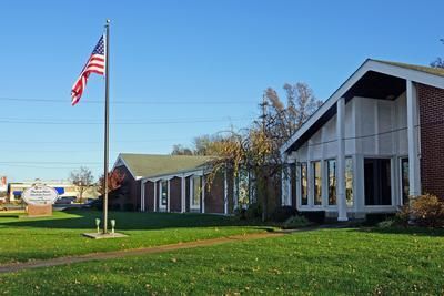 American flag waves near a brick building with large windows under a blue sky.