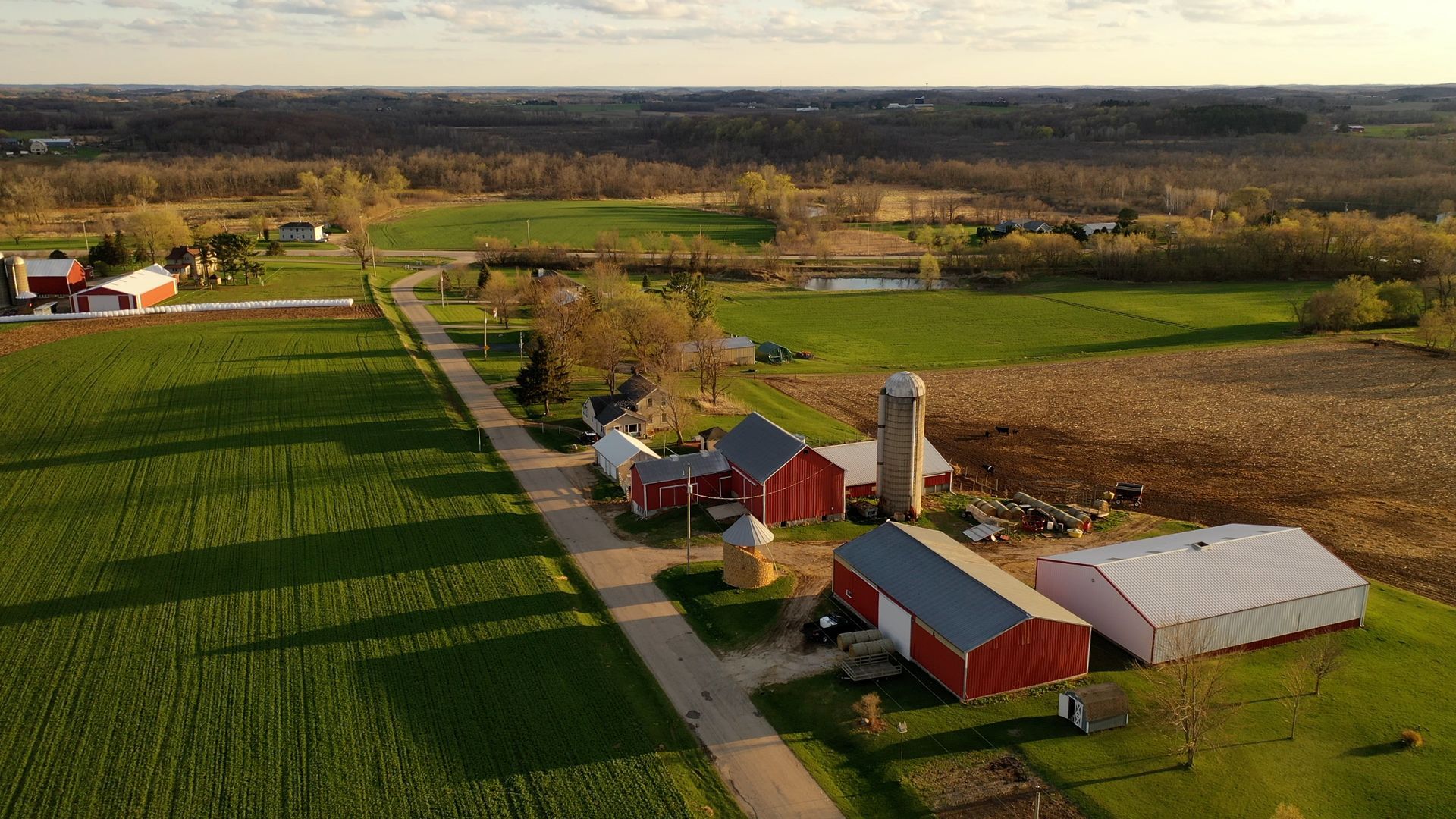 Aerial view of a farm with red barns, silos, and fields of green and brown. A road runs through it.