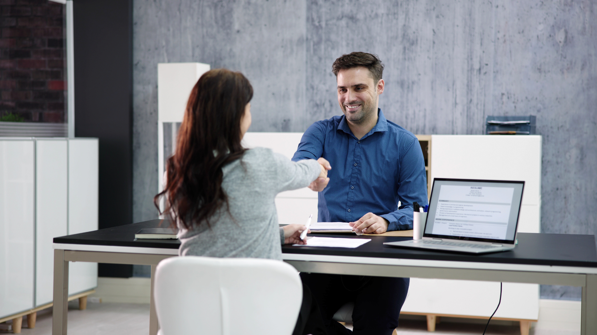 Woman shaking hands with a smiling man at a desk in an office setting.