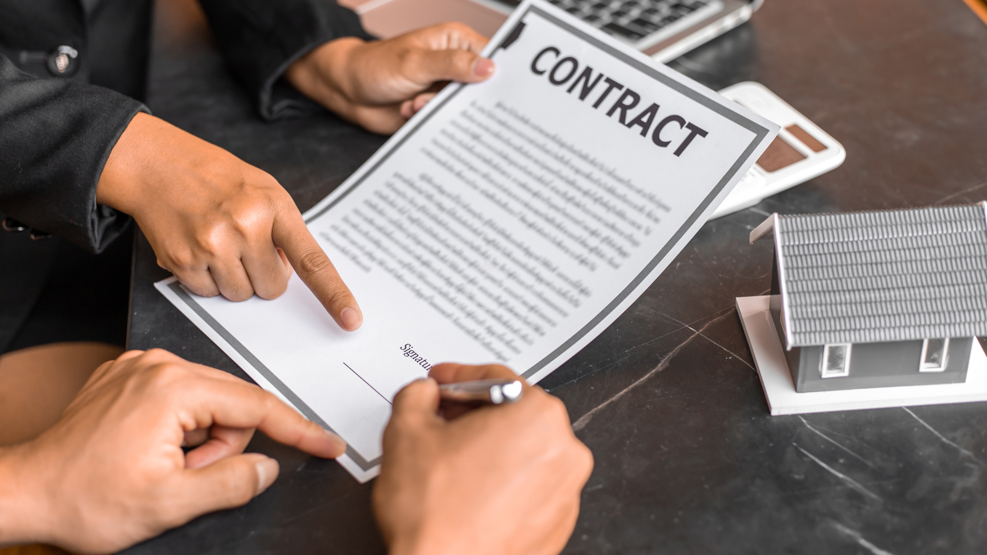 Hands pointing at a contract being signed above a miniature house; dark setting.