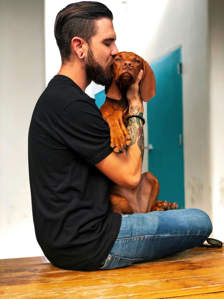 A man in a black shirt is kissing a brown dog