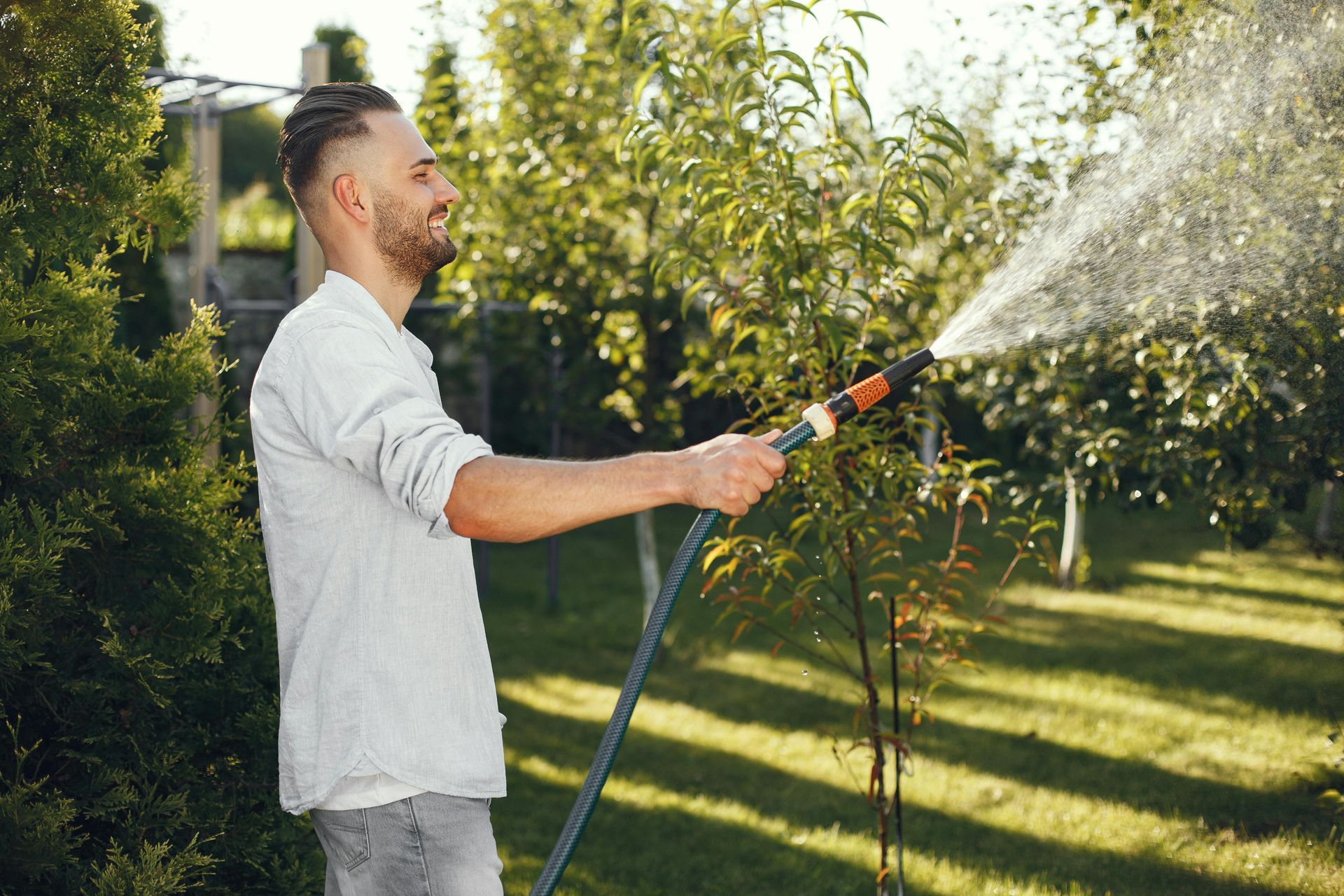 A man is watering a tree with a hose in a garden.