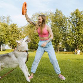 A woman is playing frisbee with a husky dog in a park.