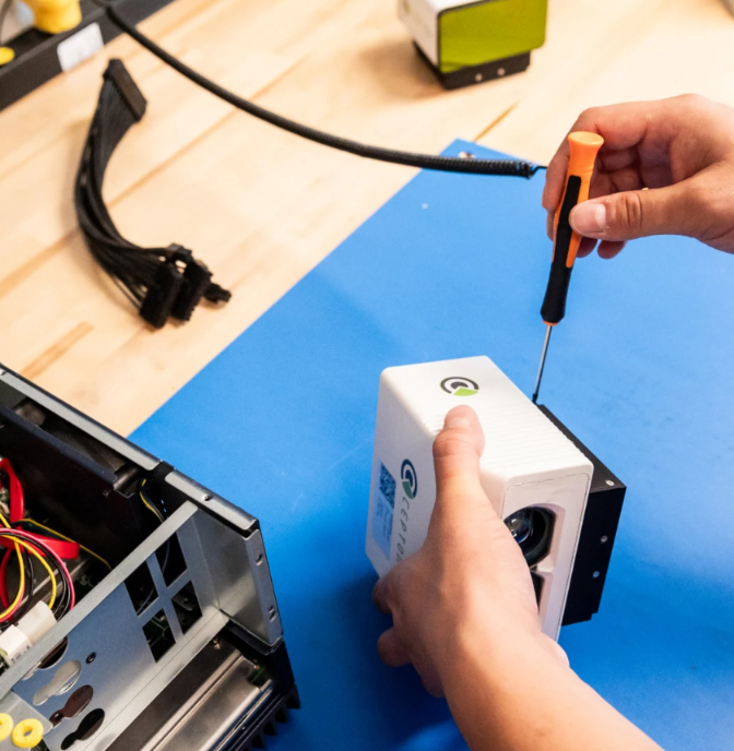 Bowler Pons staff using screwdriver on a white device with a black base on a blue surface near a computer tower.