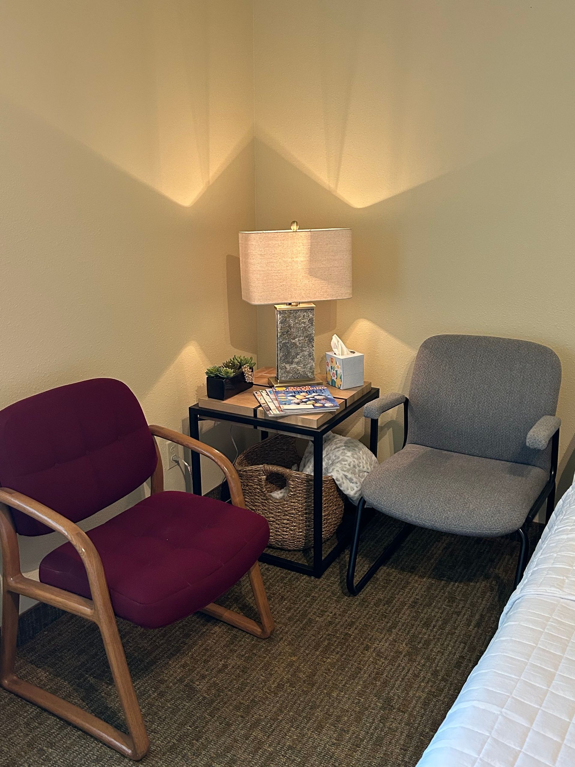 A waiting room with two chairs , a table and a lamp.