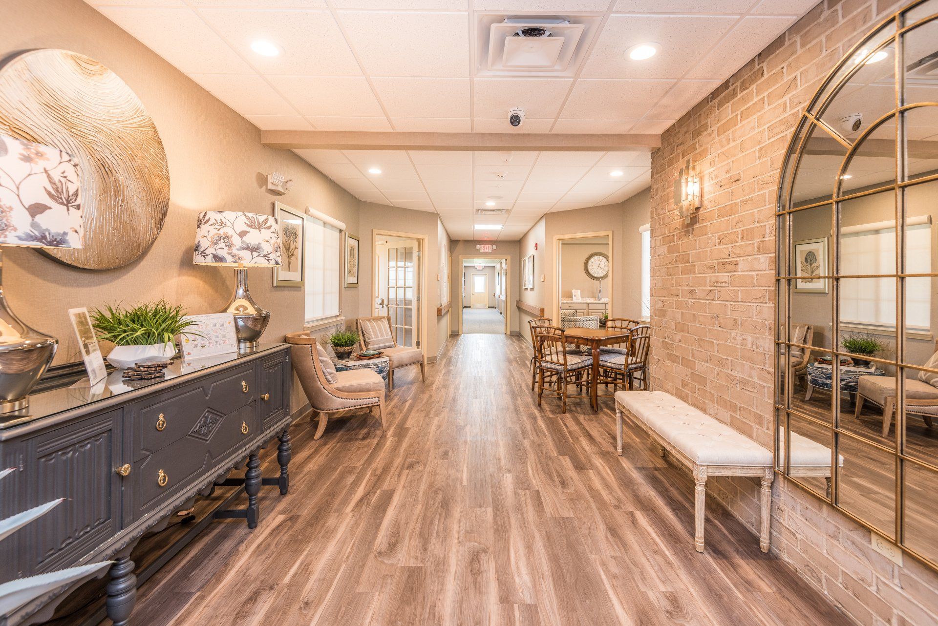 A long hallway with a dresser , chairs , a table and a mirror.