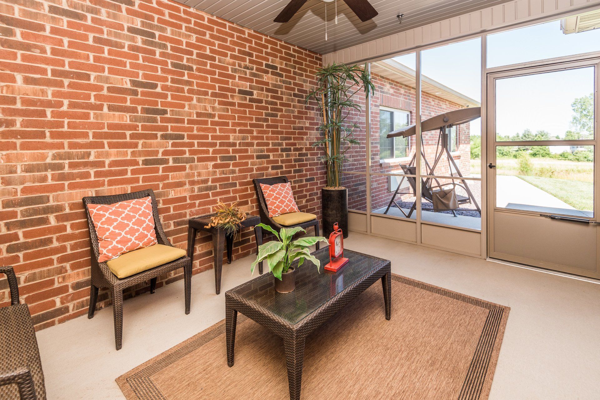 A sun room with a brick wall, chairs, a coffee table and a ceiling fan.